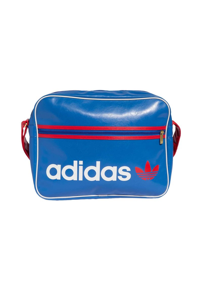 Modra torbica iz vinila z belim logotipom »adidas« in rdečimi poudarki, z žepom z zadrgo spredaj in belim obrobjem na robovih.