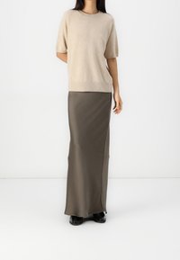 Pull beige à manches courtes en matière douce, associé à une longue jupe olive ajustée. La tenue présente un style épuré et minimaliste.