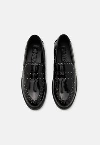 Mustat lakatusta nahasta valmistetut loafers-kengät, joissa on hopeiset niitit sivuilla. Pyöreä kärki ja litteä pohja. Kengissä on kiiltävä viimeistely ja ommeltu yksityiskohtia.