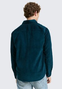Teal corduroy shirt met lange mouwen, puntkraag en knoopaccenten, met een verticale geribbelde textuur en een afgeronde zoom.
