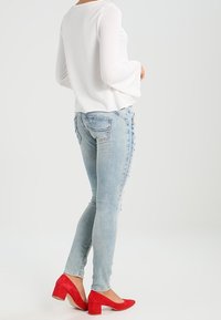 Bílý dlouhý rukáv s rozšířenými rukávy, světle modré úzké džíny s poškozeným detailem a červené semišové lodičky s blokovým podpatkem.