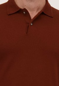 Bruine poloshirt met een zachte textuur, voorzien van een drieknoopsluiting en een kraag. De stof heeft een gladde afwerking en een getailleerd ontwerp.