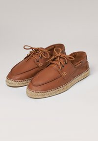 Zapatos de cuero marrón con punta redondeada, diseño con cordones y suela de yute trenzado, con acentos de costura y ojales pequeños.