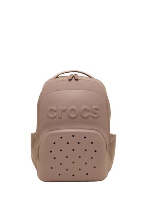 Beige Crocs rygsæk med prægede logo på toplommen og flere små, cirkulære ventilationshuller på frontlommen.