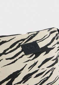 Υφασμάτινο νεσεσέρ με μπεζ φόντο και μαύρες ρίγες ζέβρας, μαύρο δερμάτινο έμβλημα λογότυπου και φερμουάρ στην κορυφή.