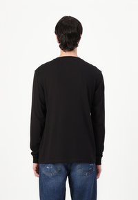 Chemise noire à manches longues dans une coupe décontractée, en tissu doux, avec un col rond et un ourlet droit, associée à un jean bleu déchiré.