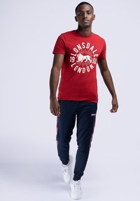 Rød kortærmet t-shirt med hvid grafik, marineblå joggingbukser med røde sidestænger og hvide sneakers. Afslappet atletisk tøj.
