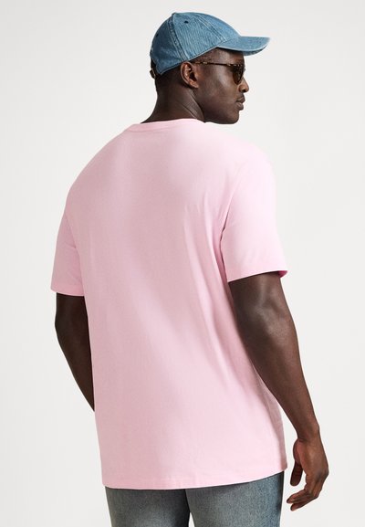 Rožinė medvilninė trumpomis rankovėmis marškinėliai su apvalia iškirpte ir laisvu siluetu, dėvimi kartu su džinsine kepure ir saulės akiniais, matomi iš nugaros.