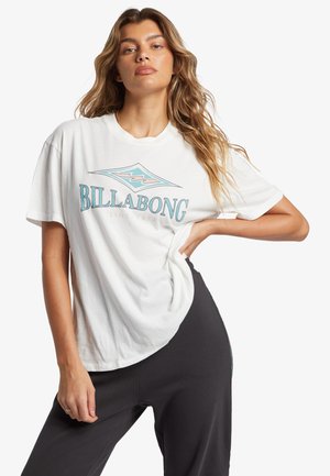 Camiseta de algodón blanca con un diseño de logo en azul y gris que incluye el texto "BILLABONG". Manga corta y corte relajado, combinada con pantalones oscuros.
