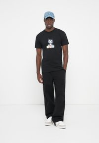 Black t-shirt featuring a cartoon character graphic with the word "HUF" in colorful blocks, paired with cargo pants and white sneakers.