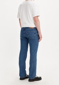 Blue denim jeans with a straight cut, featuring back pockets and a leather label on the waistband. Paired with a white short-sleeve t-shirt.