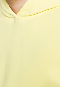 Gros plan sur un tissu jaune clair avec un col en V et un détail subtil de couture près du cou.