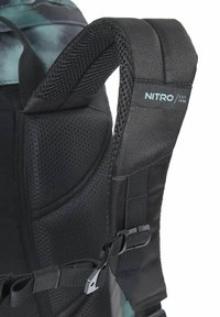 Black backpack strap with mesh padding, adjustable buckle, and branding label. Features textured fabric and a smooth surface for comfort.