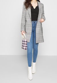 Blazer de cuadros gris con diseño estructurado, combinado con top negro y jeans ajustados azules. Botines blancos y un bolso pequeño de cuadros completan el look.