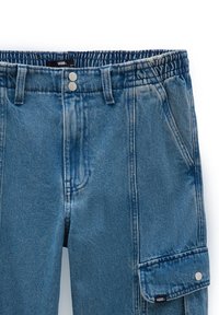 Pantalon en jean bleu avec taille élastique, fermeture par double bouton métal, poches latérales et poche à rabat avec pression sur la jambe droite.
