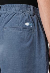 Shorts en velours côtelé bleu avec une ceinture élastique et une poche au dos avec un écusson logo Tommy Jeans. Des rainures verticales créent de la texture.