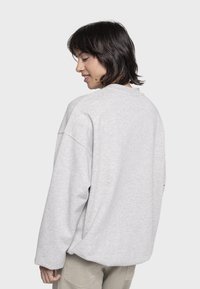 Felpa grigia oversize con spalle scese, realizzata in tessuto morbido, caratterizzata da un design semplice e un colletto a girocollo. Vista posteriore mostrata.