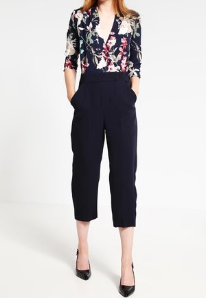 Combinaison marine à motif floral avec un col en V profond et des manches trois-quarts ; caractéristiques : pantalons larges et courts, poches latérales.