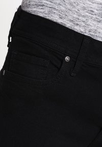 Černé džíny z denimu s úzkým střihem, designem s pěti kapsami a stříbrnými knoflíky s kontrastním prošitím na kapsách.