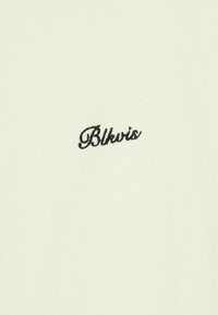 Tissu en coton couleur crème avec une texture lisse, présentant un texte noir brodé "Blkvis" près du centre.