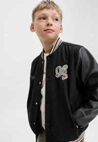 Giacca varsity nera con maniche in pelle, caratterizzata da un corpo testurizzato, colletto a righe, logo ricamato e chiusura a scatto.