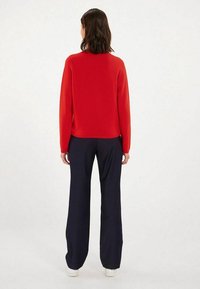 Pull en maille rouge à manches longues, coupe décontractée, associé à un pantalon large bleu marine et des baskets blanches. Texture lisse et design simple.