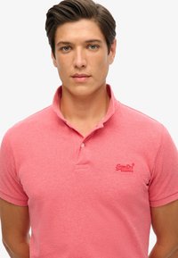 Camiseta polo roja con un tejido texturizado, cuello y tapeta de tres botones. Presenta un pequeño logo bordado en el pecho.