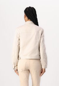Light beige denim jacket with a straight cut, button closures, and minimal stitching details, shown from the back with matching pants.