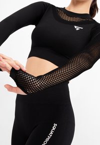 Schwarzes, langärmliges Sportoberteil mit einem Mesh-Design an Schultern und Ärmeln, ergänzt durch passende, hochgeschnittene Leggings mit Logo-Akzenten.