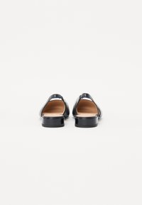 Chaussures en cuir verni noir avec un dos ouvert, un petit talon carré et un intérieur lisse. Le design présente des lignes épurées et peu de détails.