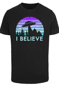 Black cotton t-shirt featuring a UFO graphic above mountain silhouettes. The design includes a gradient circle in purple and blue with text "I BELIEVE" in aqua.