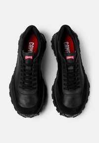 Black leather sneakers with textured surface, rubber soles, and black laces. Red "CAMPER" logo on a black tongue. Rounded toe design.