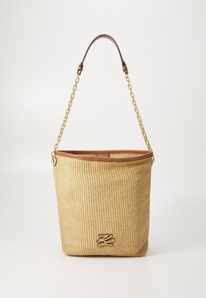 Beżowa pleciona torba typu bucket z brązowymi skórzanymi wykończeniami, złotym łańcuszkiem jako paskiem oraz metalowym emblematem z logo z przodu.