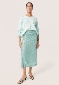 Top verde menta con vestibilità ampia e dettagli legati sulle maniche, abbinato a una gonna midi fitted in paillettes verde menta. Sandali neri con cinturini.