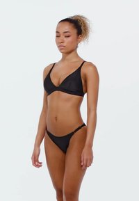 Černý dvoudílný bikini plavky vyrobené z hladké látky; top má trojúhelníkové košíčky a tenké ramínka, zatímco spodní díl má klasický tanga střih.