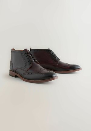 Tamsiai rudos ir burgundinės odinės brogue tipo aulinės botai, su sparnuotuoju dizainu, brogue dekoro detalėmis, apvalia nosimi ir raištelių uždarymu.