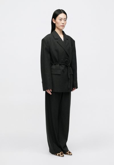 Fekete csíkozott, oversize blézer, amelyhez passzoló, széles lábú nadrágok és leopárd mintás, hegyes orrú cipők tartoznak. Az anyag texturált hatású, struktúrált dizájnnal rendelkezik.