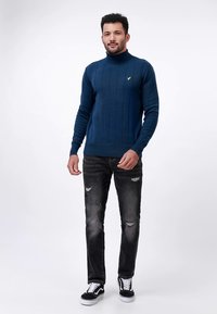 Navyblauer, gestrickter Rollkragenpullover mit geripptem Muster, kombiniert mit zerrissenen schwarzen Jeans und schwarz-weißen Sneakern.