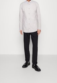 Helles, gestreiftes Button-Up-Hemd mit Kragen und langen Ärmeln, kombiniert mit schwarzen Hosen und glänzenden schwarzen Schnürschuhen.