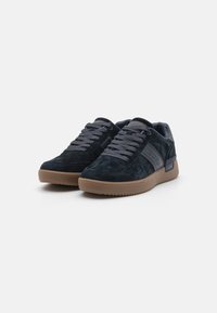 Sapatilhas de camurça azul-marinho com atacadores cinzentos e solas de borracha; apresentam um logo lateral e gola acolchoada para conforto.
