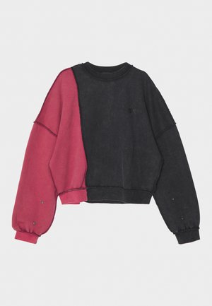 Crop sweatshirt featuring a black body with a pink left sleeve. Loose fit, round neckline, and contrasting stitching details.