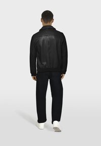 Chaqueta de cuero negra con cuello, dobladillo acanalado y detalle de costura en la espalda, combinada con pantalones oscuros y zapatillas blancas.