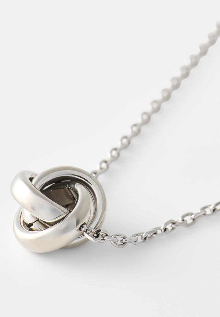 Zilveren metalen ketting met een knoopvormige hanger met een glad oppervlak, ingewikkeld verweven ontwerp en een delicate ketting.