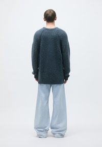 Oversized dark blue textured sweater with long sleeves, paired with loose light blue denim pants. Sweater features raglan sleeves and a relaxed fit.