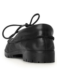 Scarpa in pelle nera con una forma arrotondata, caratterizzata da un profilo basso e una suola in gomma testurizzata. Dettaglio con lacci legati sul retro.