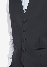 Schwarze formelle Weste mit fünf Knopfverschlüssen, mit Schwalbenschwanzkragen und glatter Textur. Getragen über einem hellblauen Hemd.