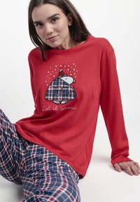 Top de manga larga rojo con un oso bordado en una manta de cuadros que dice "Deja que nieve". Combinado con pantalones de pijama de cuadros en azul marino y rojo.