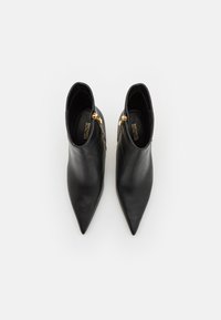 Bottes noires en cuir jusqu'à la cheville avec un bout pointu, détail de fermeture éclair dorée sur le côté, présentant une texture lisse et une silhouette épurée.