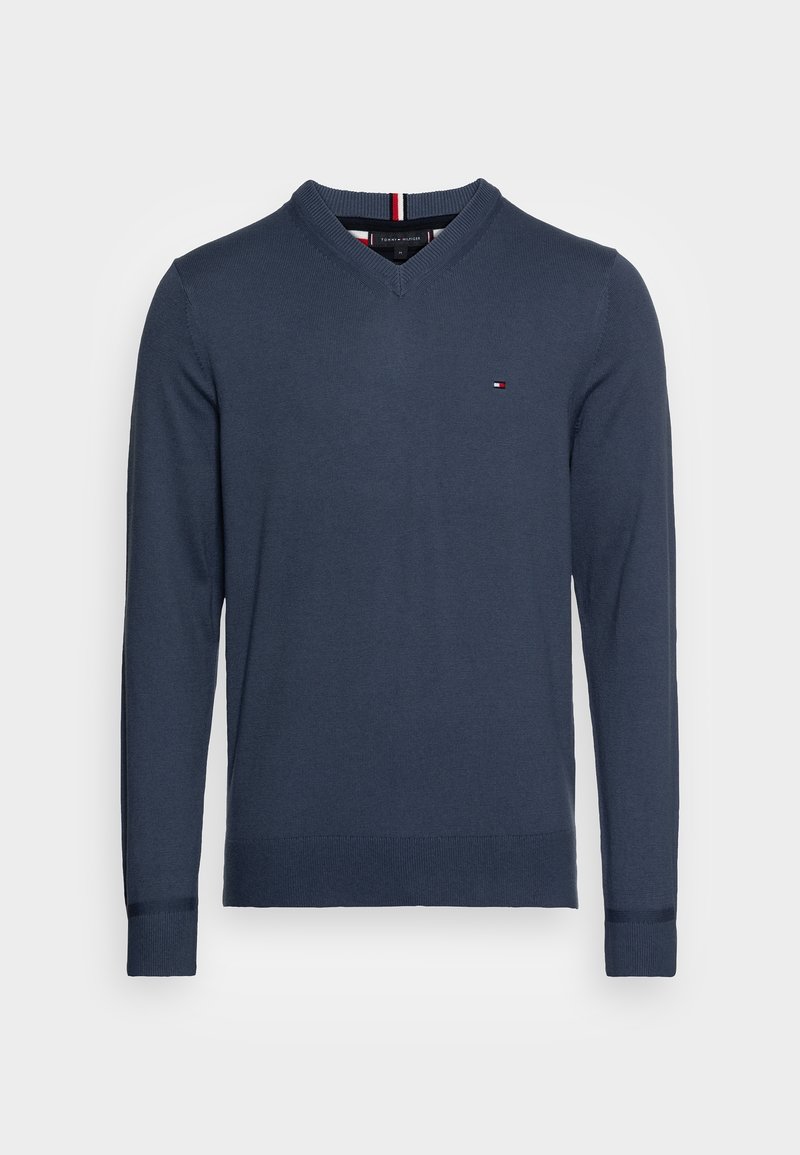 Pull à manches longues bleu marine à col en V avec petit logo Tommy Hilfiger sur le côté gauche de la poitrine et poignets et ourlet côtelés.