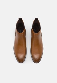 Chaussures en cuir marron sans lacets avec des bouts arrondis et des panneaux latéraux élastiques noirs, vues de dessus sur un fond blanc.